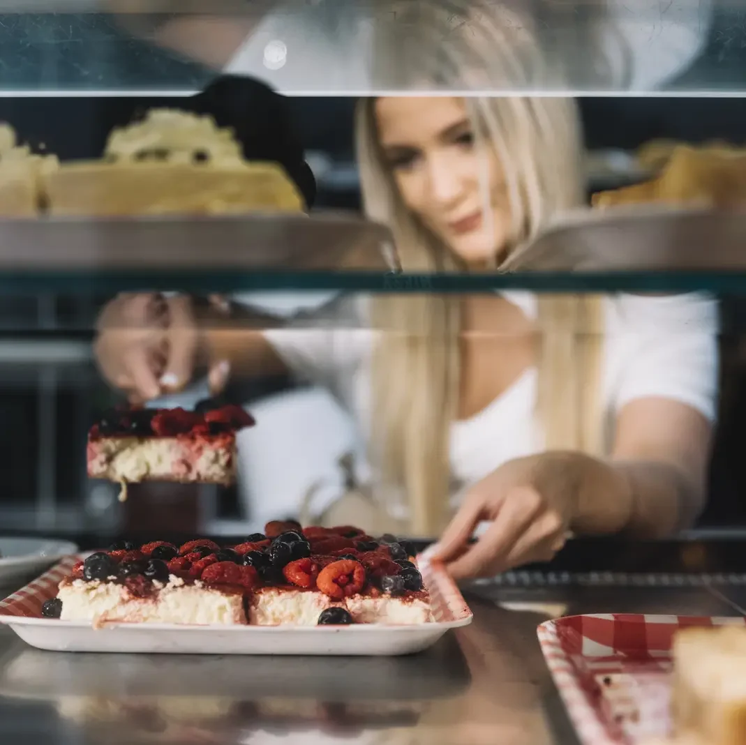 Shop assistant holding pastry from a refrigerated display - Frost Flare