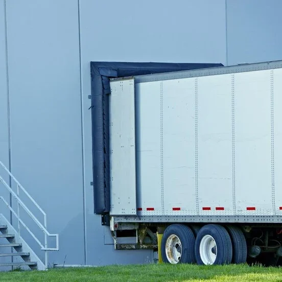 A semi-truck with a refrigerated trailer docked at a warehouse.