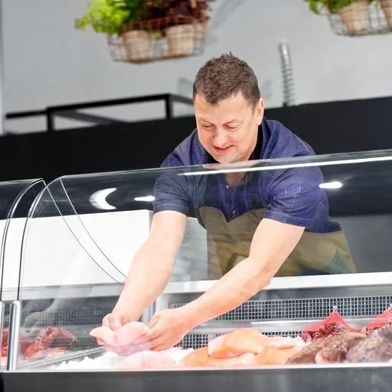 A man arranging fresh seafood in a display fridge by Frost Flare with a glass door, showcasing various types of fish and seafood in a retail setting.